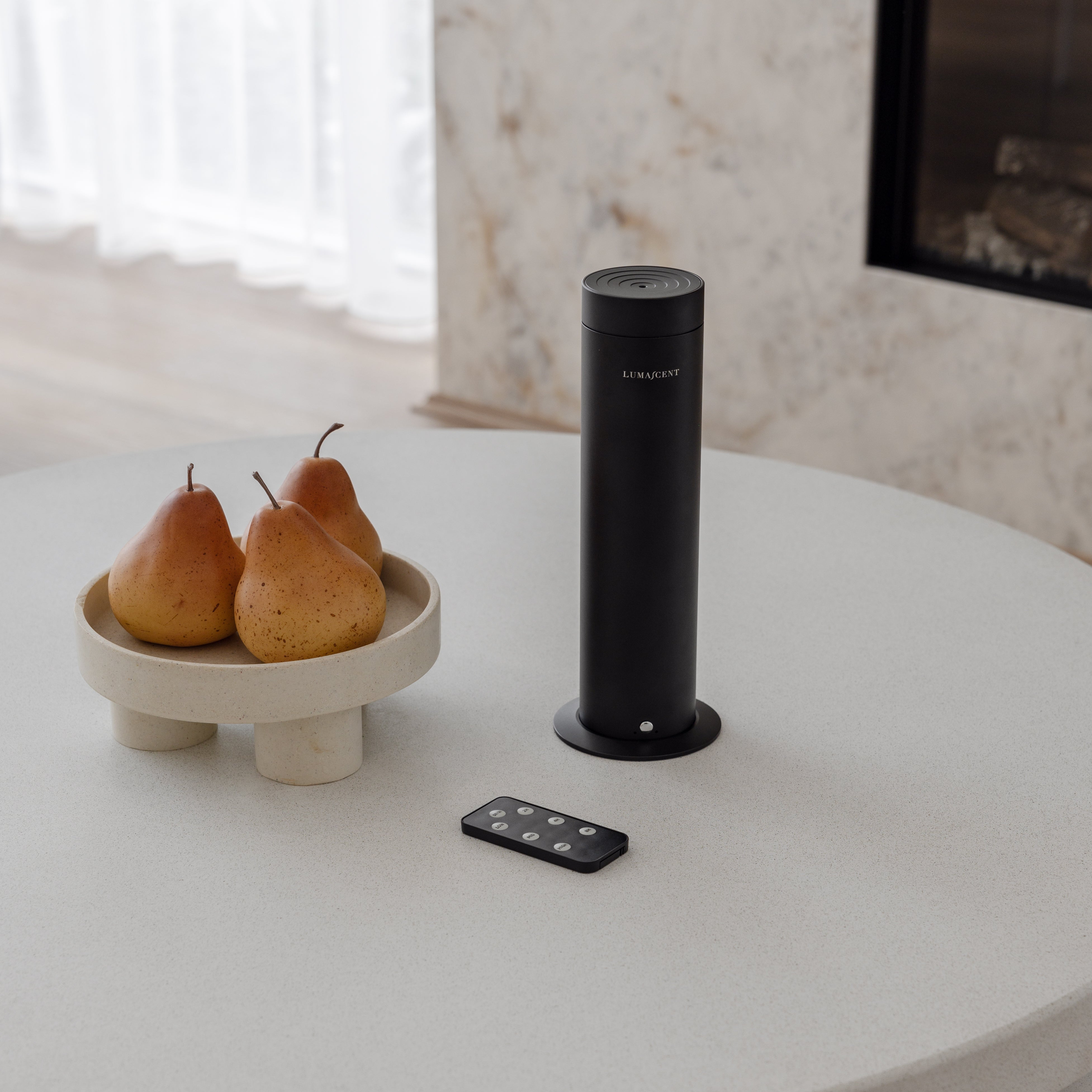 Black cylindrical device on a white table with pears and a remote control.